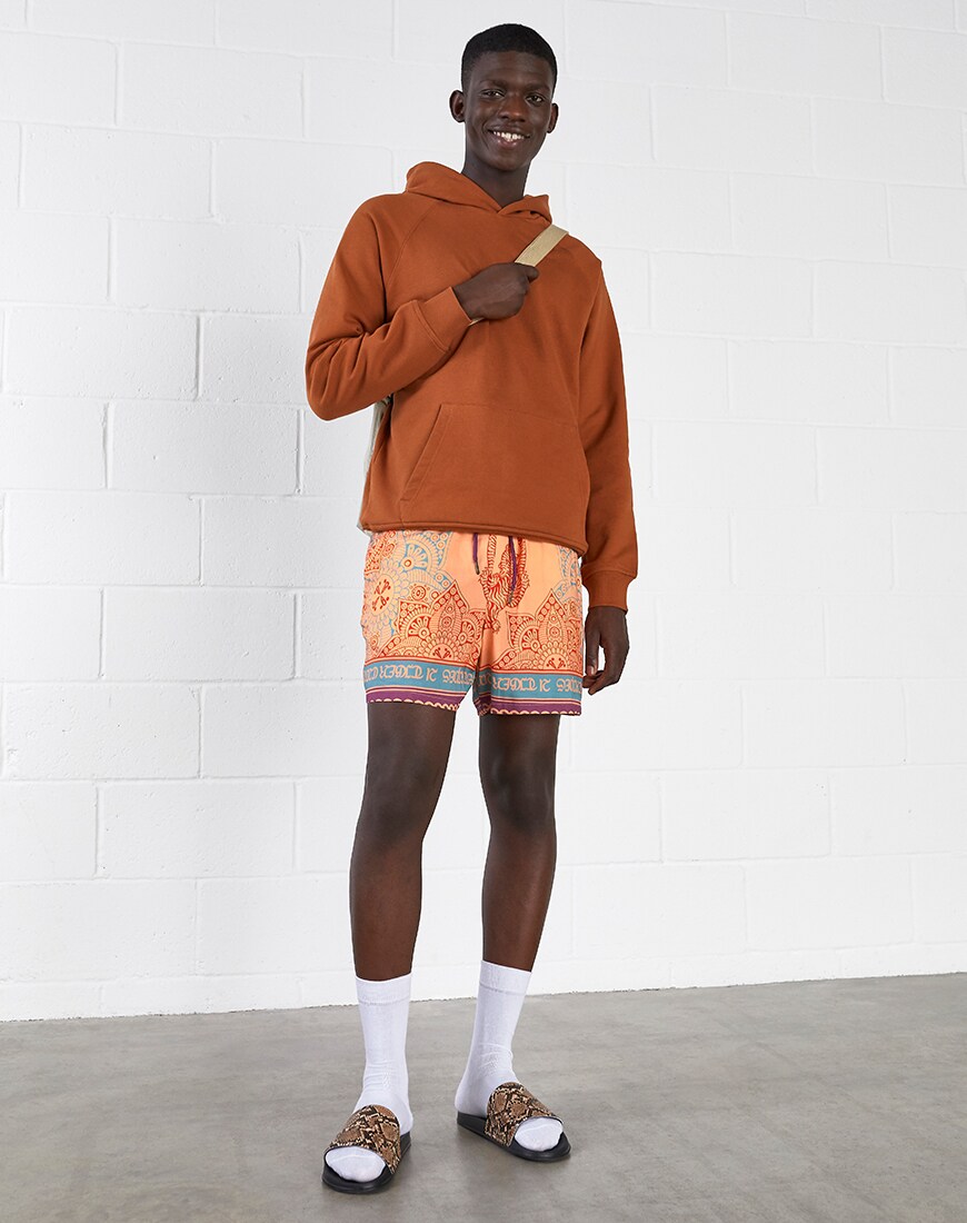 A picture of a model wearing a rust-coloured hoodie, printed shorts and leopard-print sliders. Available at ASOS.