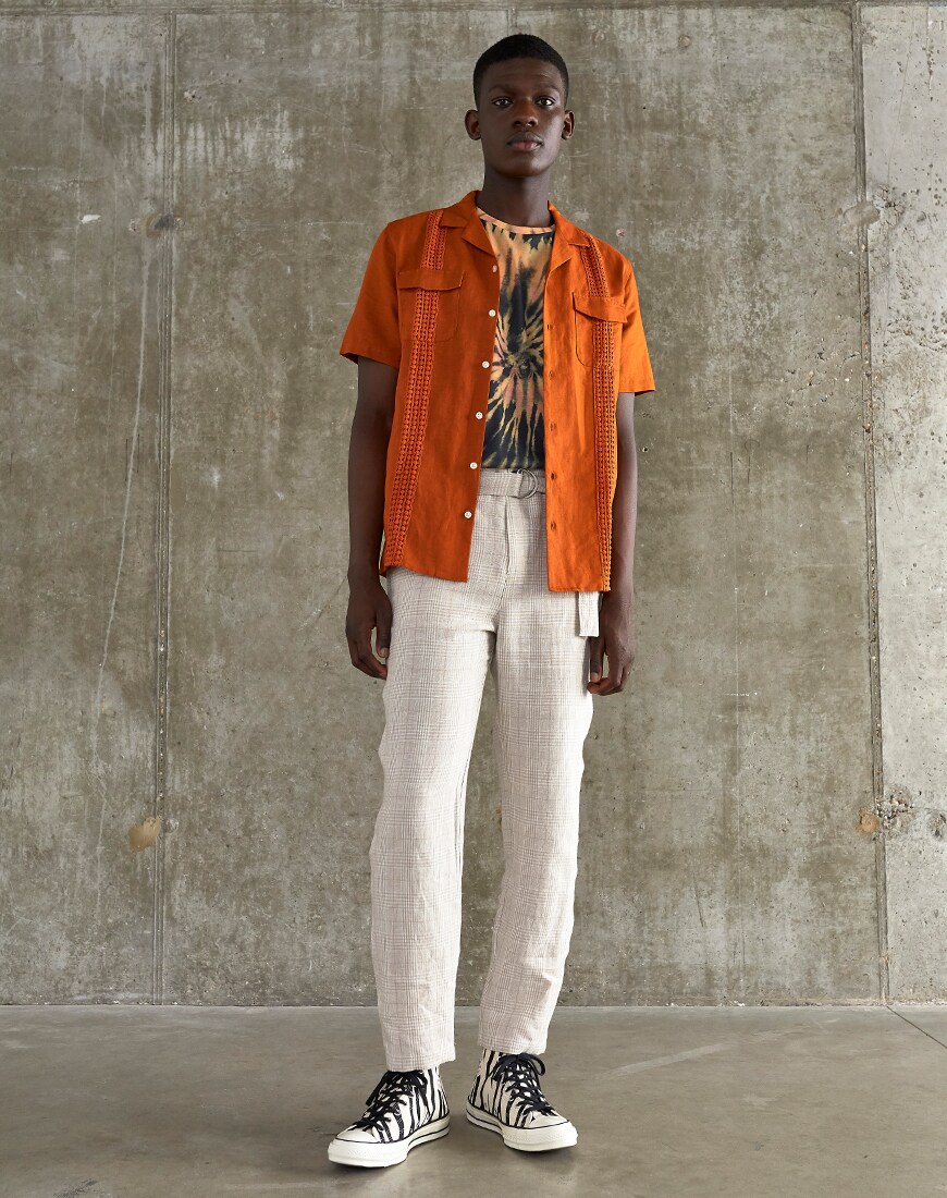 A picture of a model wearing a crochet shorts-sleeve shirt, a tie-dye T-shirt and check trousers. Available at ASOS.