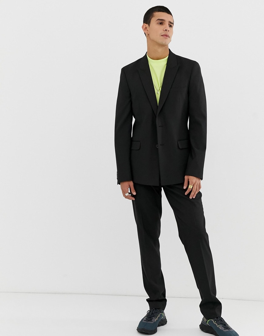 A picture of a model wearing a black suit with a T-shirt and trainers.