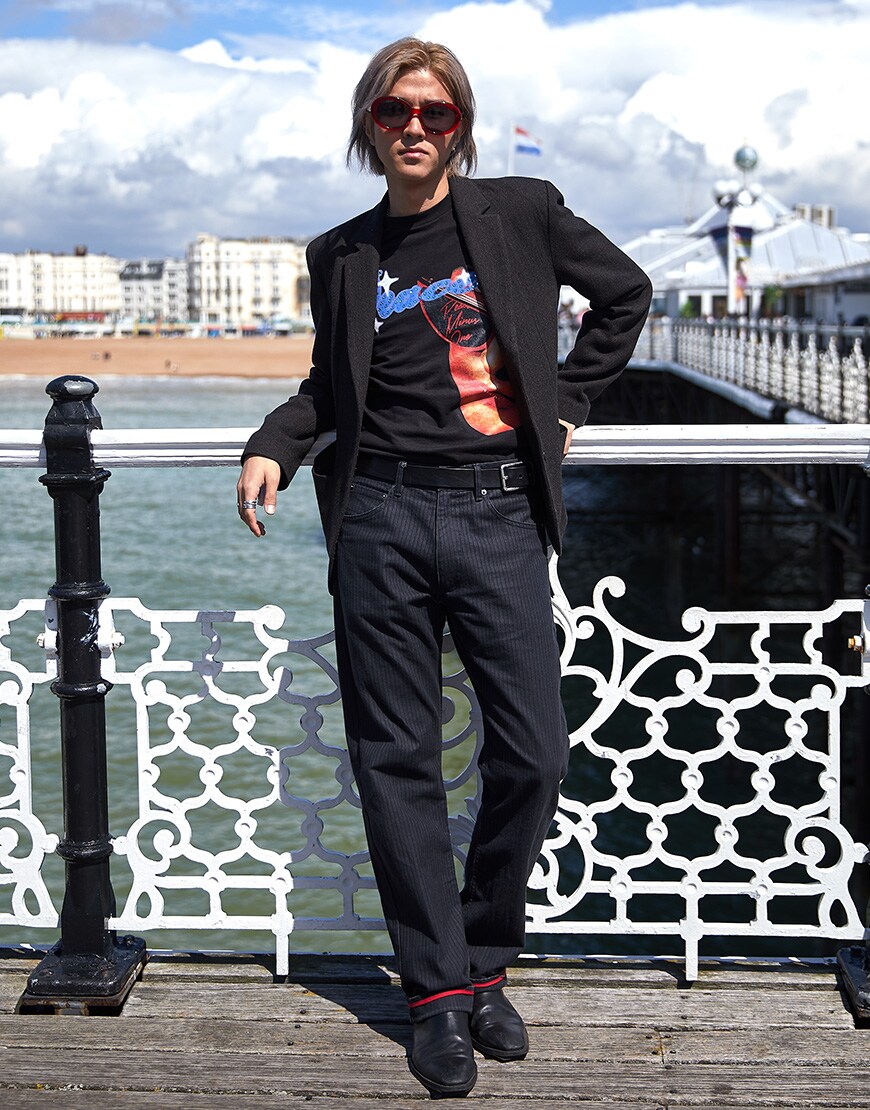 A picture of a man wearing a blazer and jeans with a band T-shirt and sunglasses.