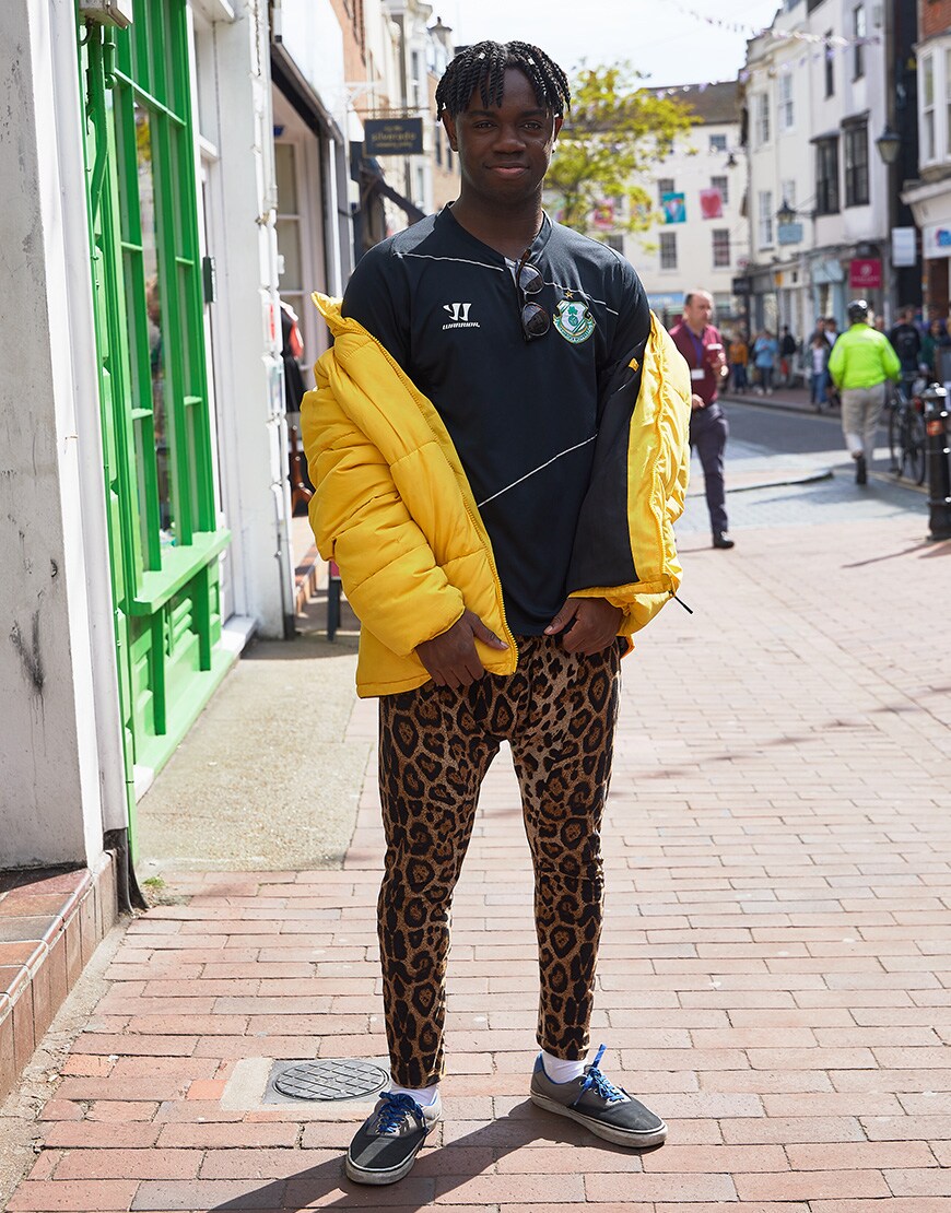 A picture of a man wearing a football shirt, a bright-yellow puffer jacket and leopard-print leggings.
