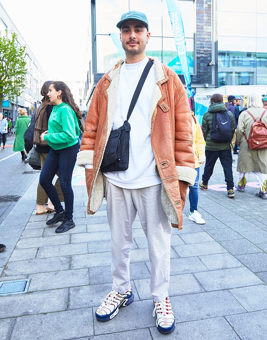 A picture of a man wearing a shearling coat, a white sweatshirt and lilac trousers.