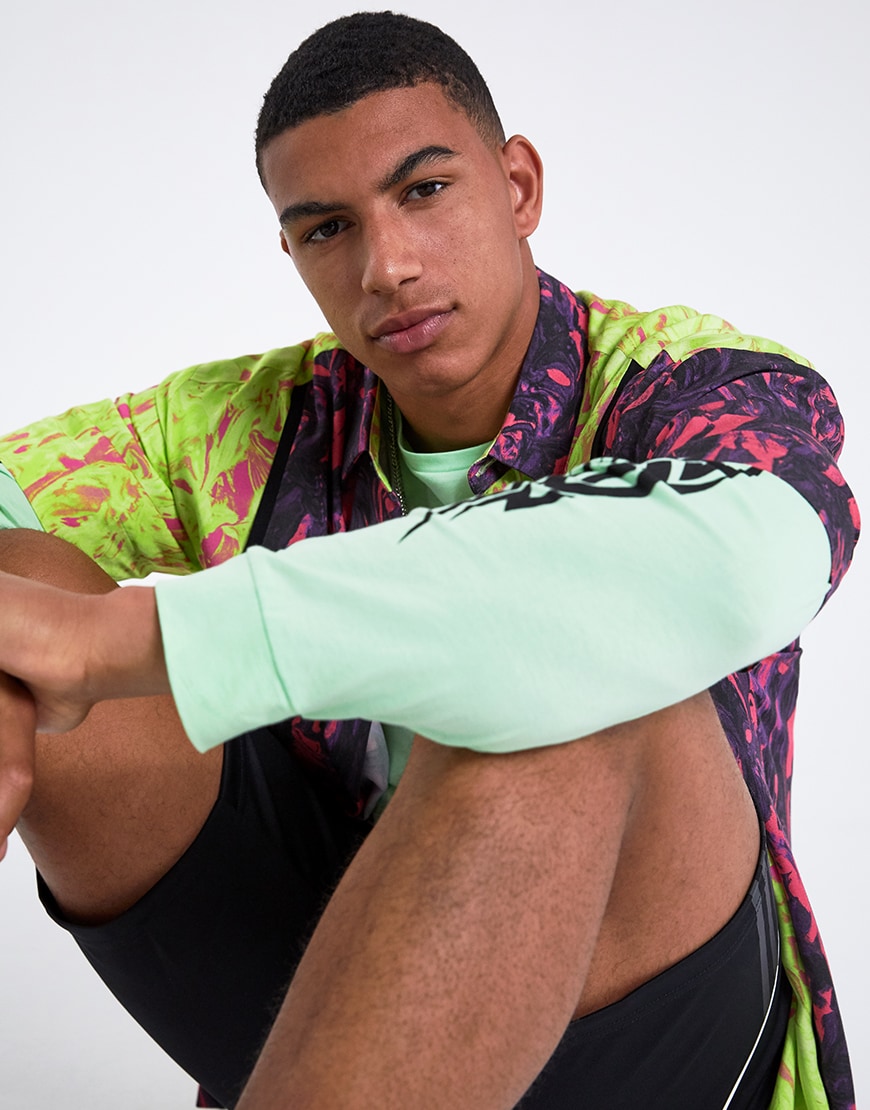 A picture of a model wearing a neon shirt, a long-sleeve 90s-style tee and adidas shorts. Available at ASOS.