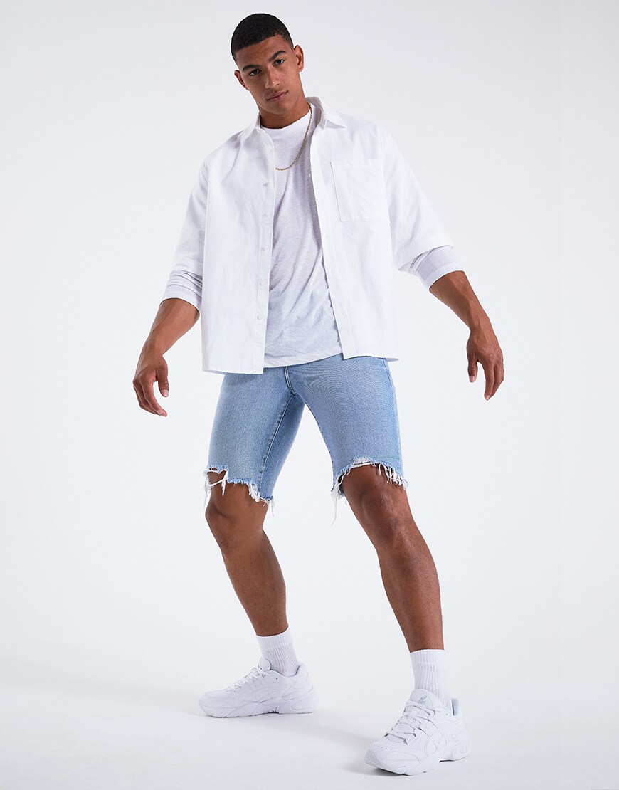 A picture of a model wearing a white short sleeve shirt over a white long-sleeve tee, ripped denim shorts and Ascics trainers. Available at ASOS.