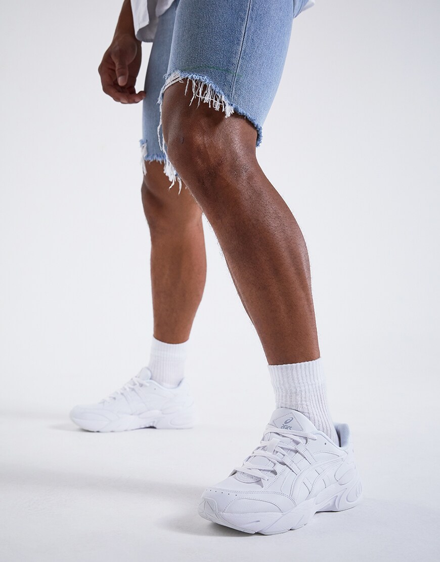 Image d'un modèle portant une chemise à manches courtes blanche sur un t-shirt à manches longues blanc, un short en jean déchiré et des baskets Asics. Disponible chez ASOS.