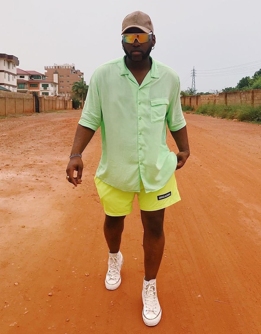 A picture of a man wearing and neon green shirt, visor-style sunglasses and yellow shorts.