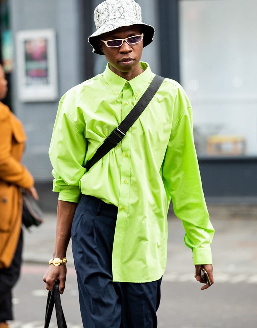 A picture of a man wearing a snake-print bucket hat, 90s-style sunglasses and a neon shirt.