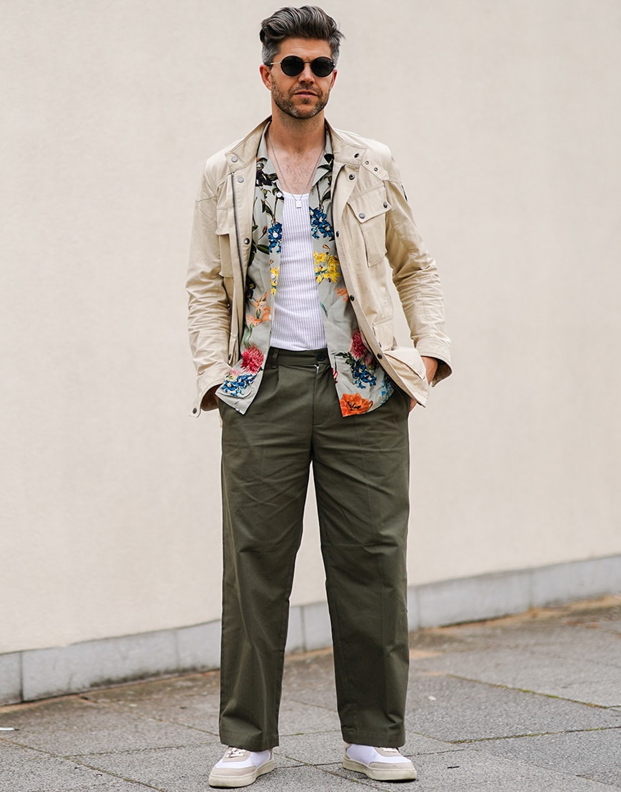 A picture of a man wearing wide-cut trousers, a floral shirt and an overshirt.