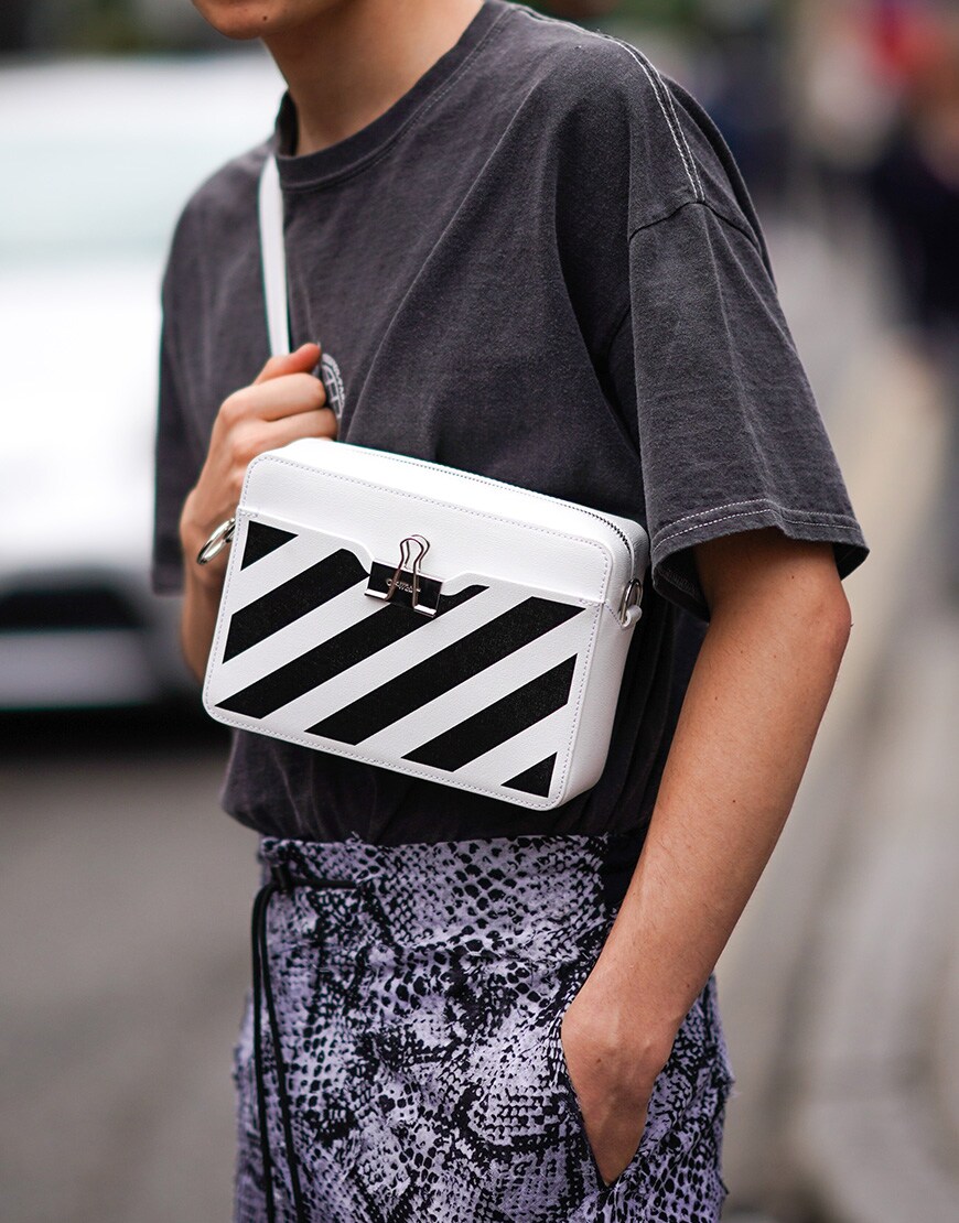 A pciture of a man wearing a striped cross-body bag and snake-print trousers.