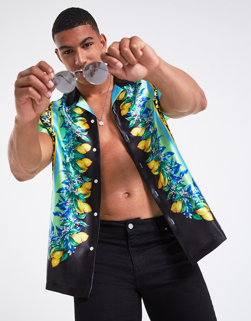 A picture of a model wearing a fruit-print shirt, sunglasses, denim shorts and black trainers. Available at ASOS