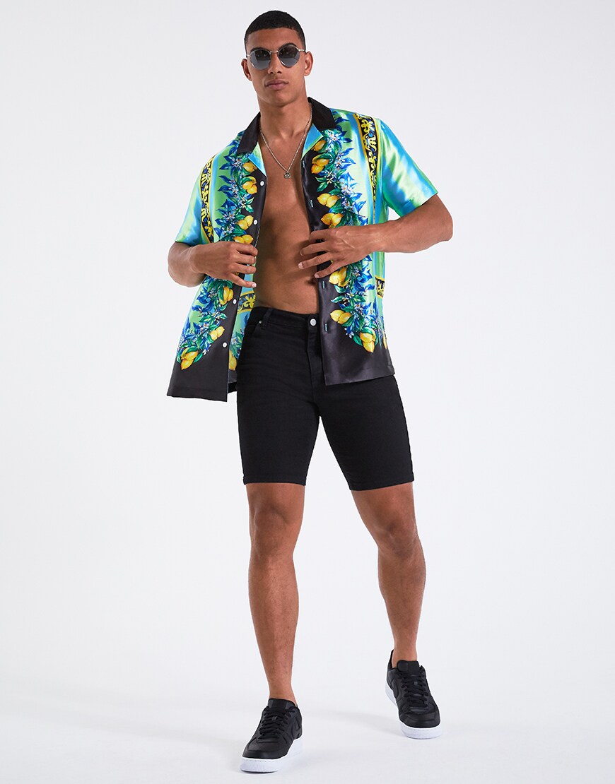 A picture of a model wearing a fruit-print shirt, sunglasses, denim shorts and black trainers. Available at ASOS.