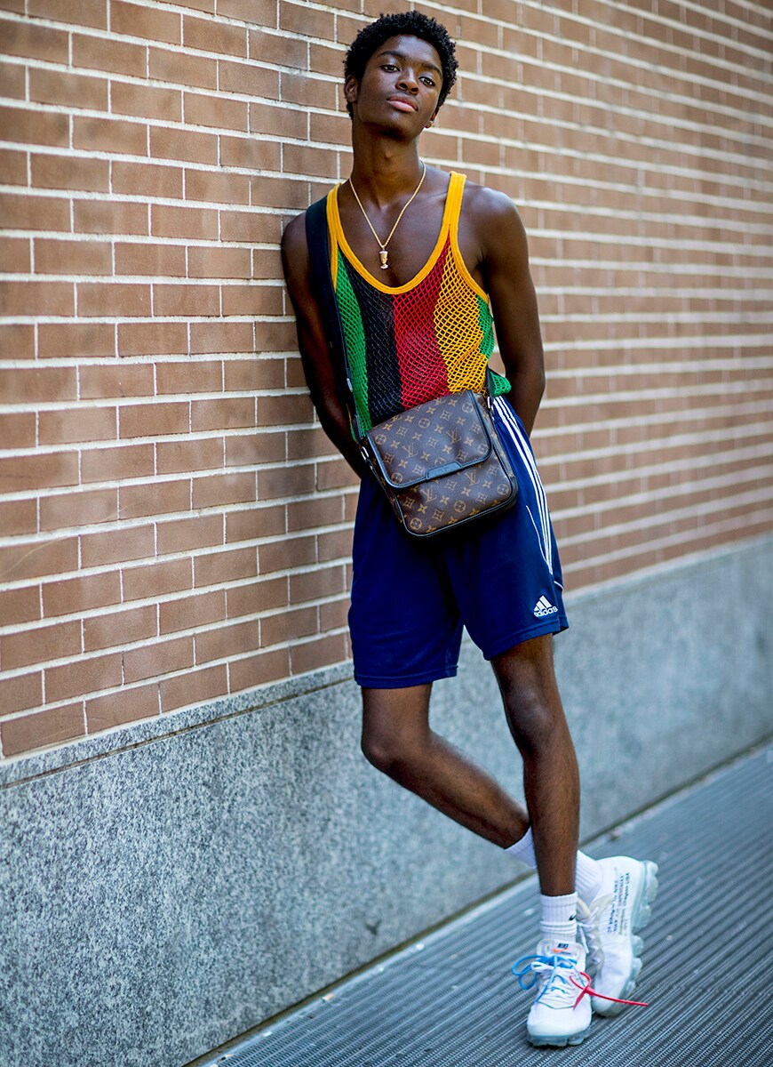 A picture of a man wearing a mesh vest, adidas shorts and a cross-body bag.