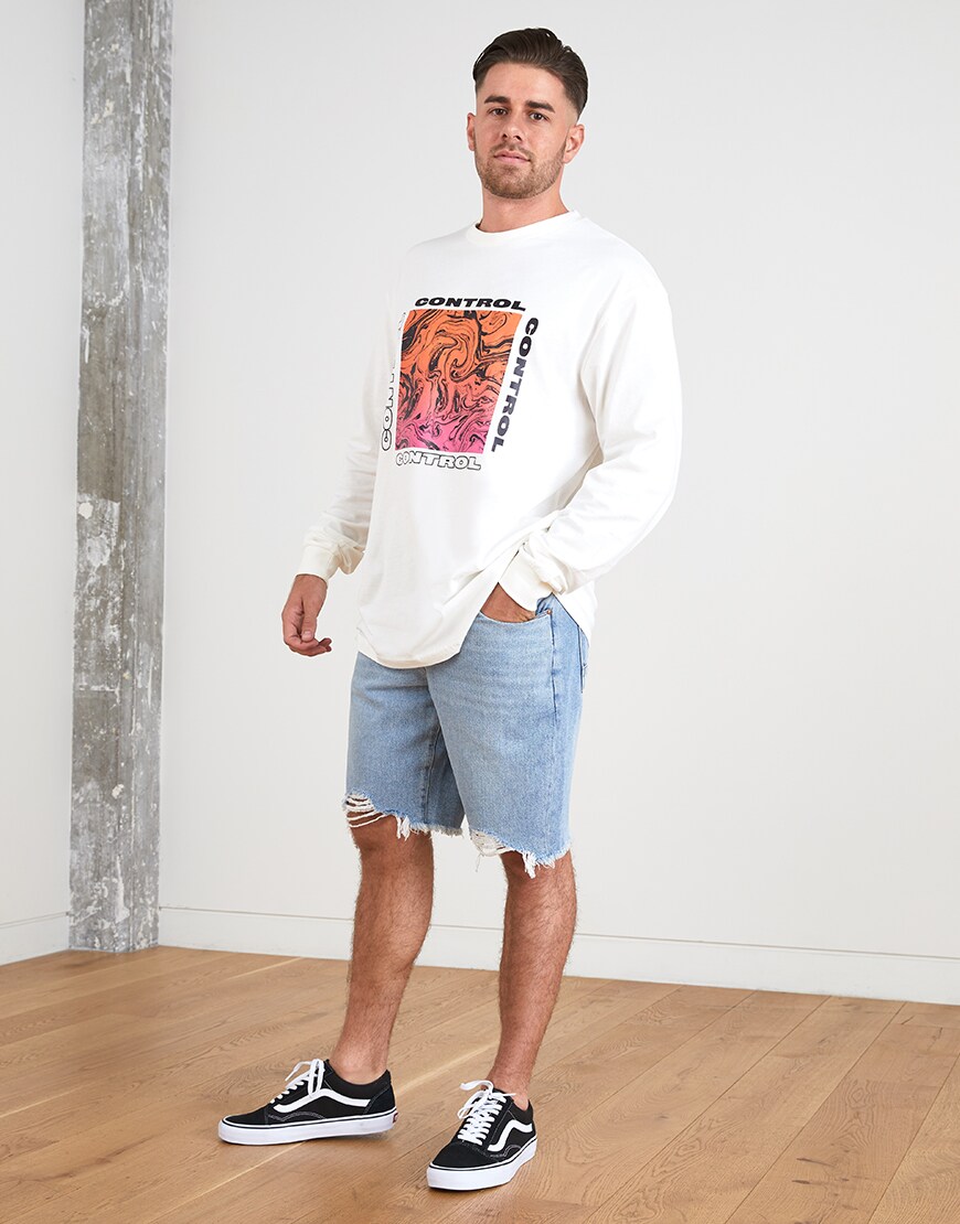 A picture of an ASOSer wearing a long-sleeve graphic T-shirt and ripped denim shorts. Available at ASOS.