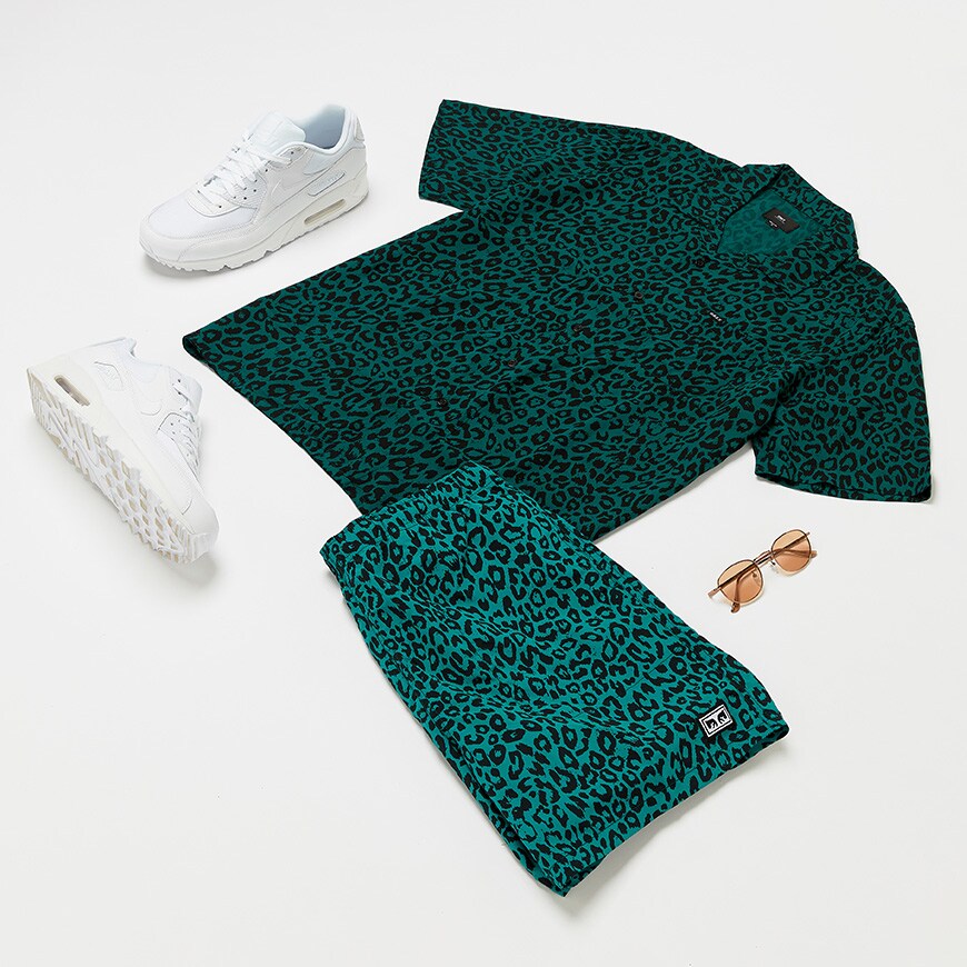 A flat lay picture of a green leopard-print co-ord from Obey with sunglasses and Nike Air Max trainers. Available at ASOS.