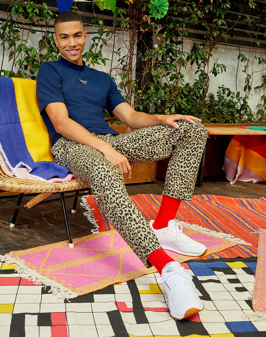 A picture of a model wearing a Reebok T-shirt, leopard print chinos and Reebok Classic Leather trainers. Available at ASOS.