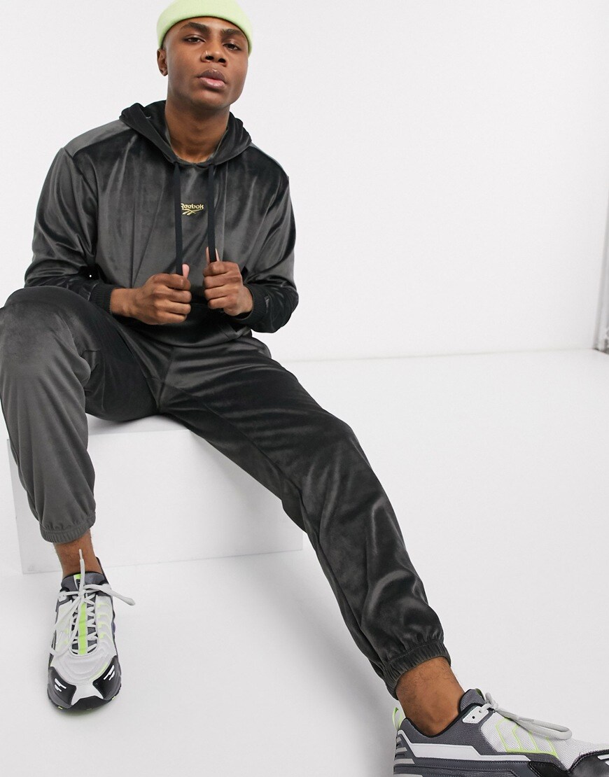A picture of a model wearing a neon-green beanie with a black velour hoodie and joggers by Reebok. Available at ASOS.