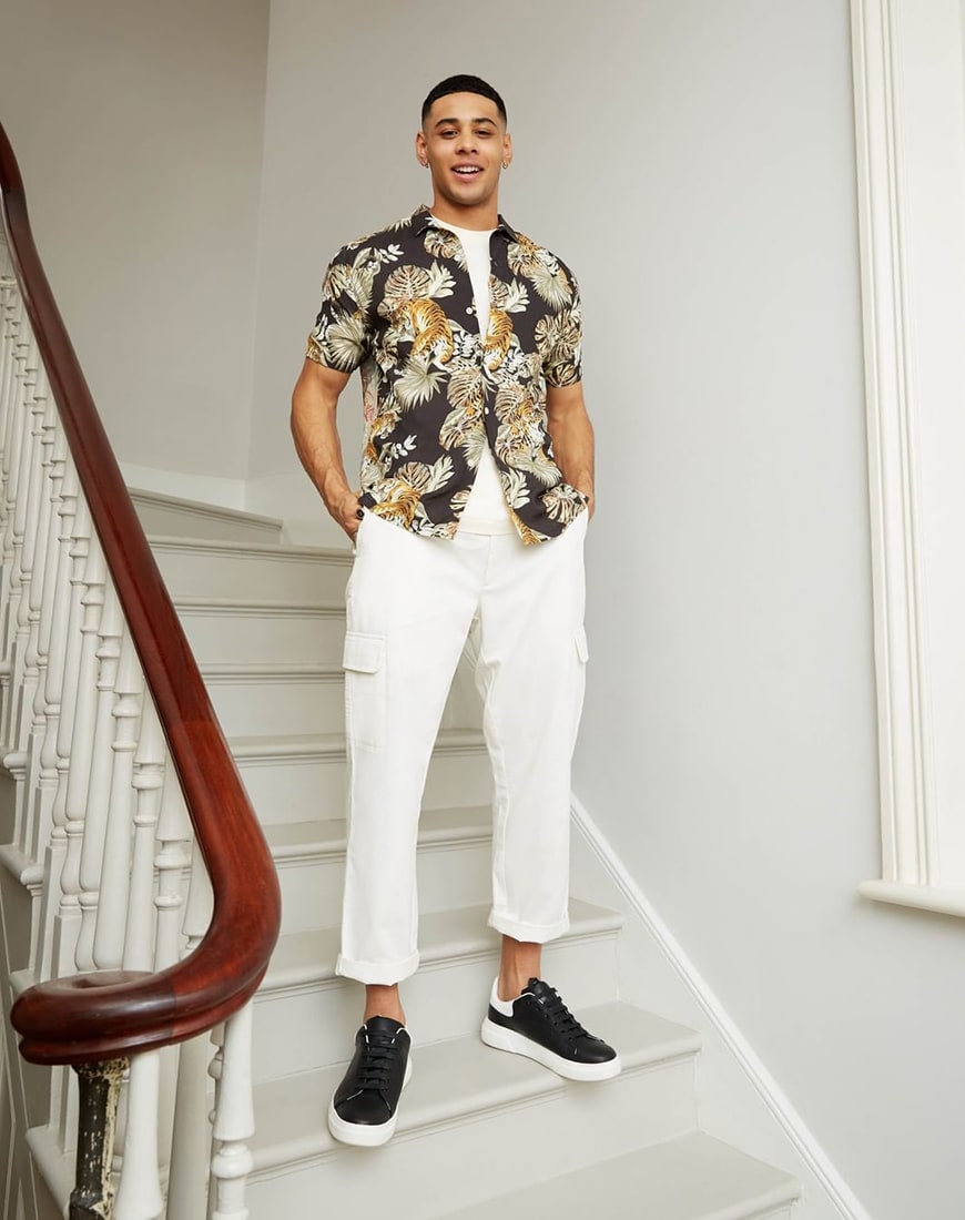 A picture of a man wearing a printed shirt by Topman and white cargo trousers. Available at ASOS.Alternate Text