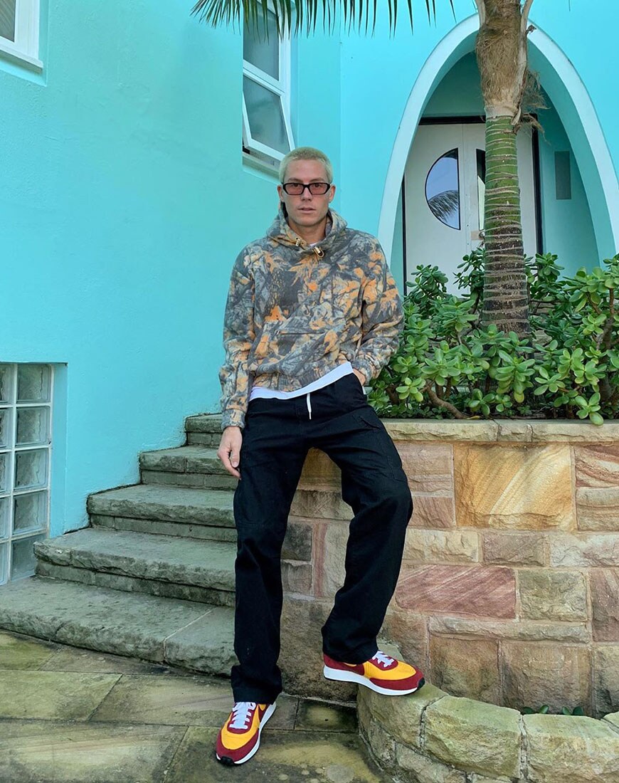 A picture of an ASOS Insider, asos_jono wearing a colourful camouflage hoodie with black cargo trousers and Nike trainers.