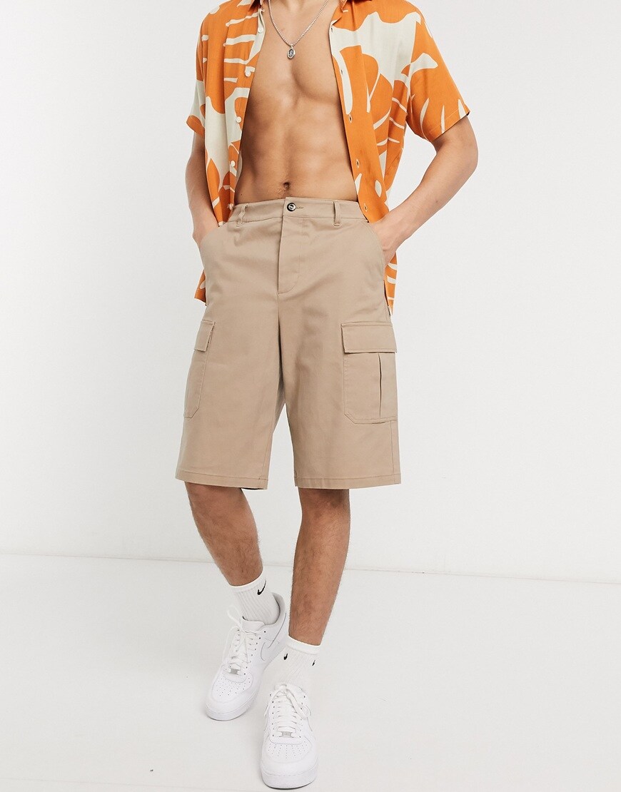 A picture of a model wearing a pair of stone-coloured cargo shorts cut in a longer length that sits on the knee. Part of the ASOS Responsible Edit and available now.