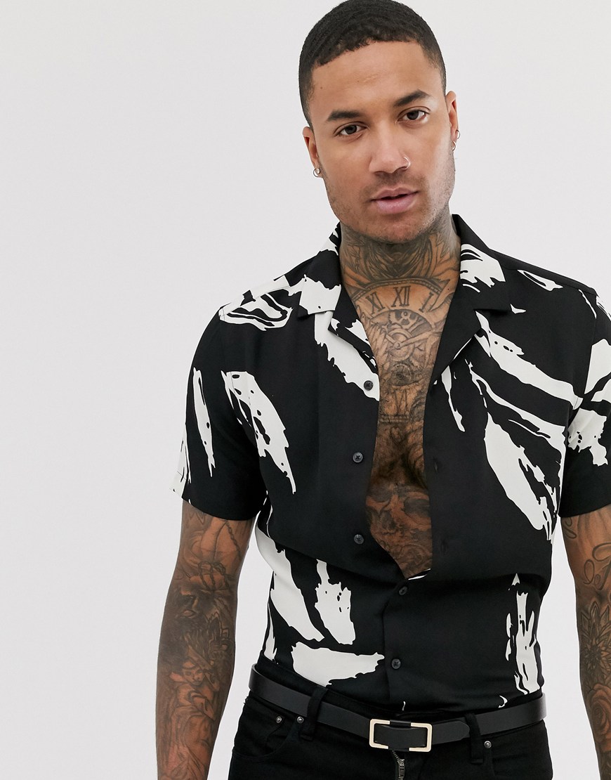 A picture of a model wearing a revere collar shirt from the ASOS Responsible edit. It features an abstract leaf print in a black and white colourway. Available now.