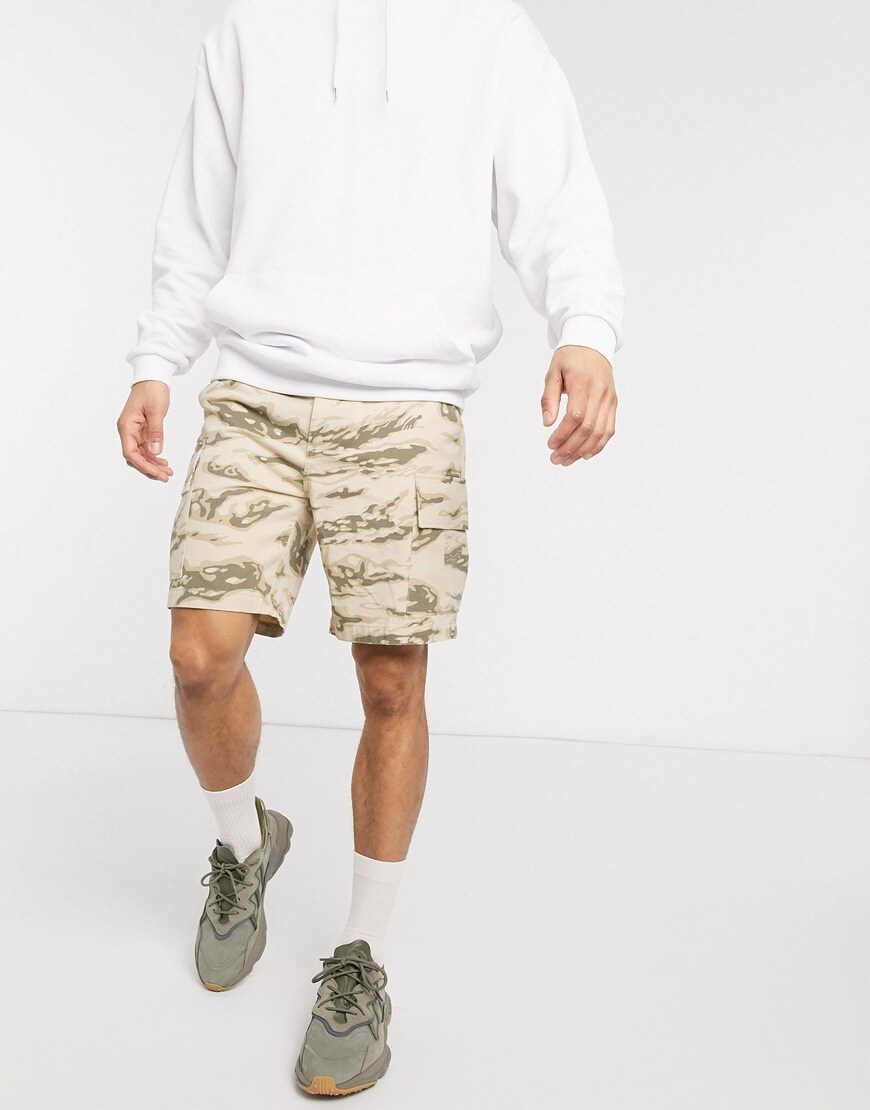A picture of a model wearing beige camo-print shorts by Reclaimed Vintage. Available at ASOS.
