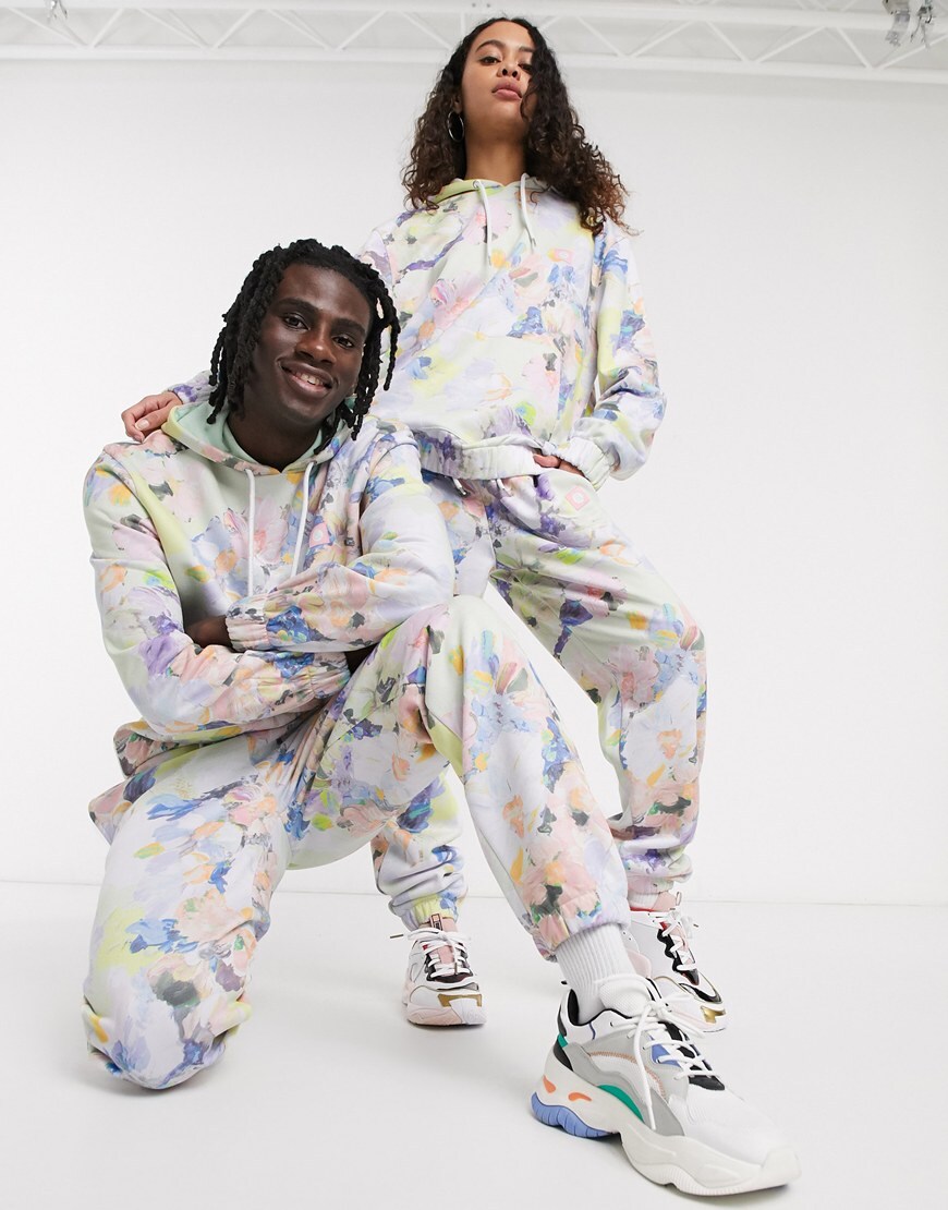 A picture of a male and female model wearing a bright floral print hoodie and joggers co-ord. They are part of the new ASOS X GLAAD collaboration. Available now.