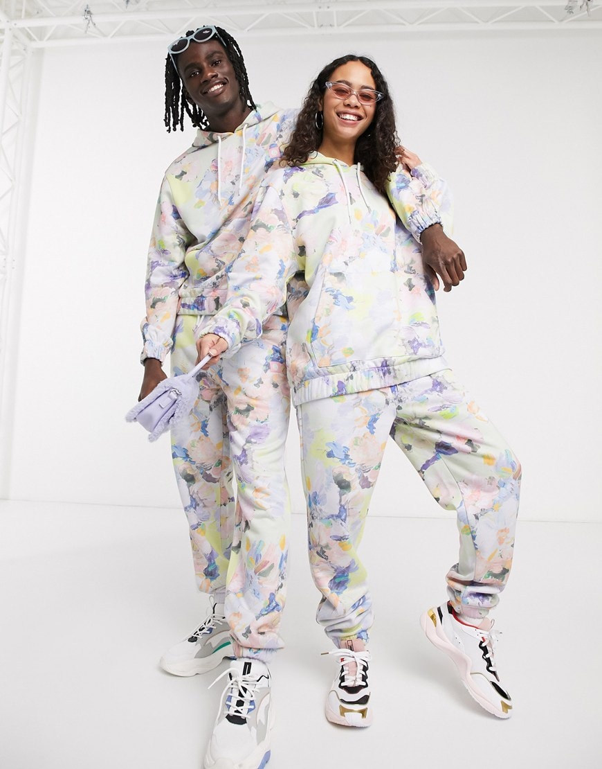 A picture of a male and female model both wearing a brightly coloured hoodie and joggers co-ord set featuring a bright floral print. Part of the new ASOS X GLAAD collaboration. Available now.