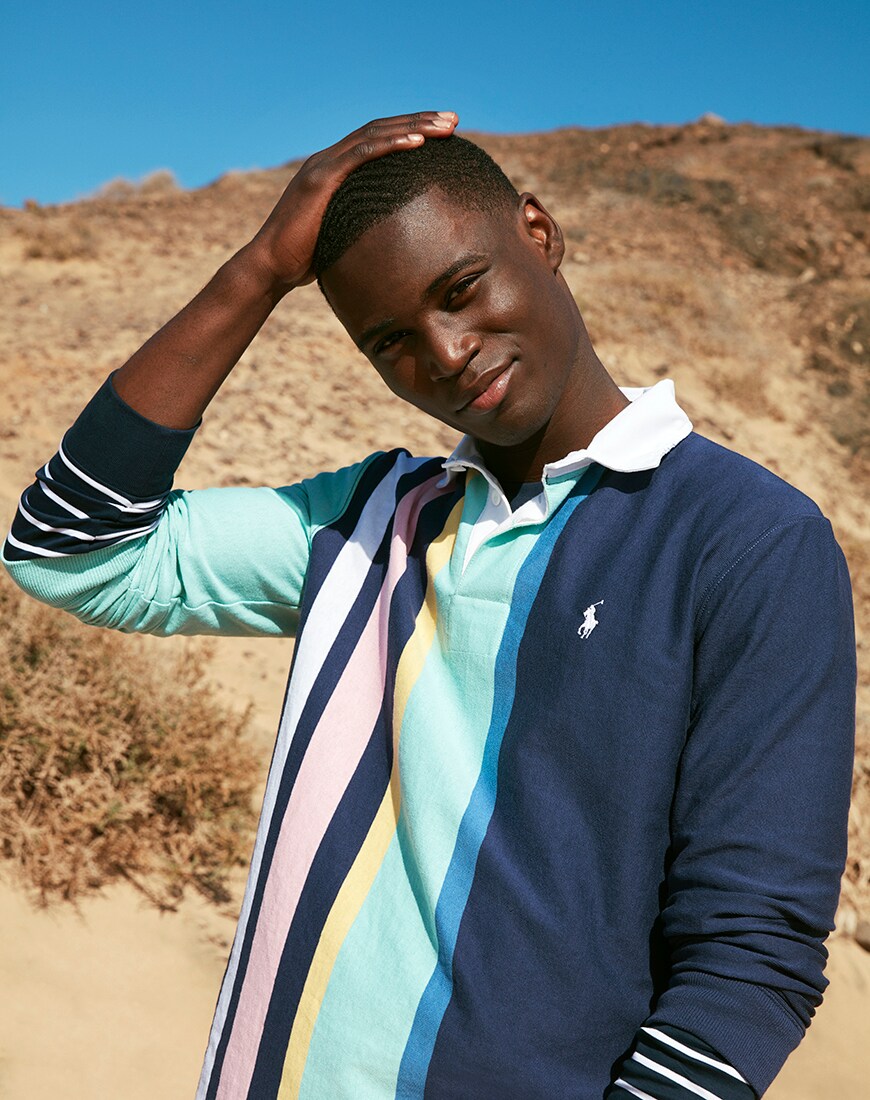 A picture of a model wearing a navy rugby top with pastel stripe details from the new and exclusive Polo Ralph Lauren capsule collection. Available now.