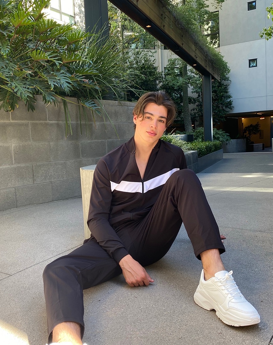Pierre sitting in a navy blue matching tracksuit and white trainers | ASOS Style Feed