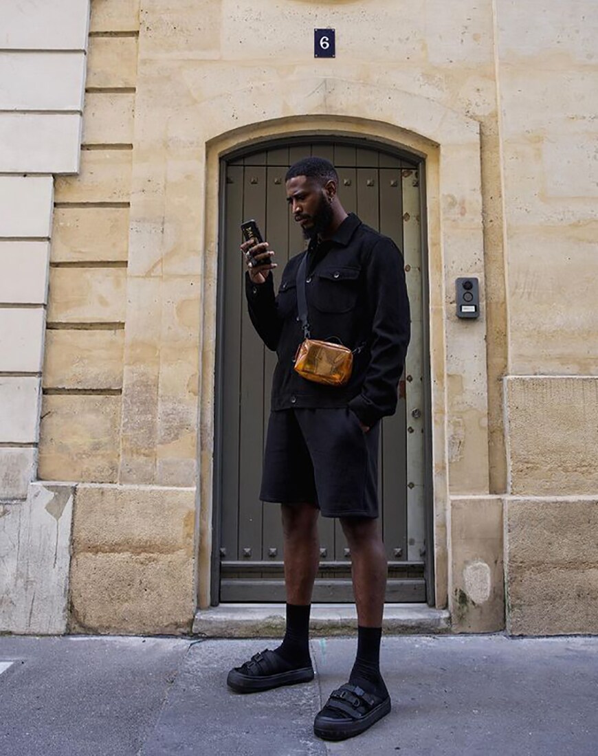 A man wearing a denim jacket, t-shirt, shorts, socks and sliders all in black | ASOS Style Feed