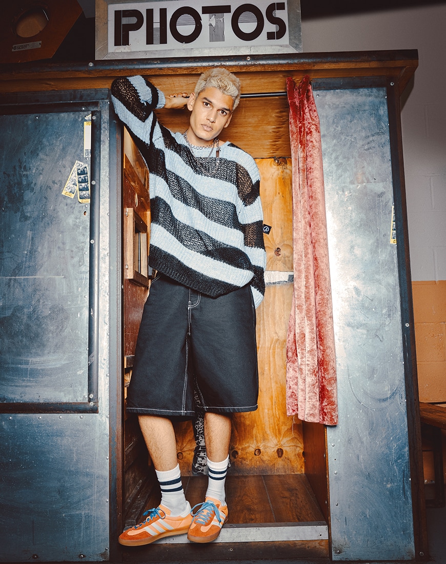 A man wearing a striped jumper and oversized denim shorts