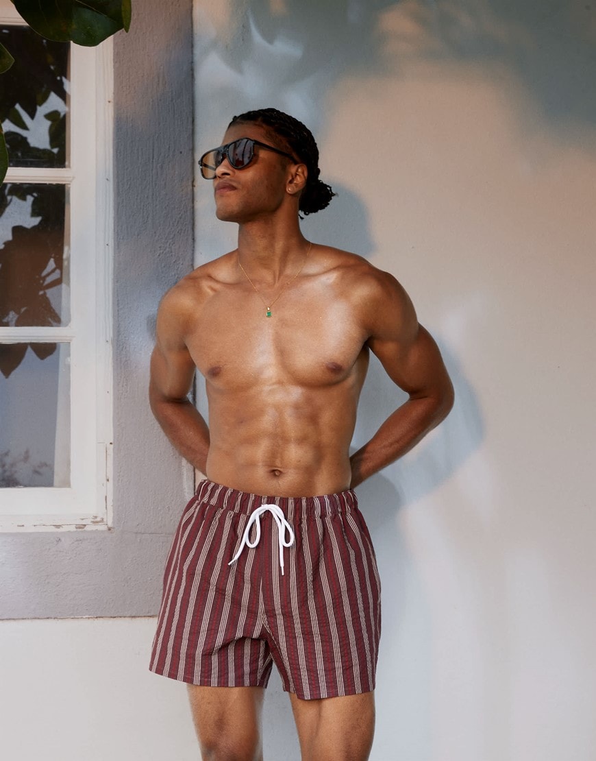 A model wearing burgundy striped swim shorts