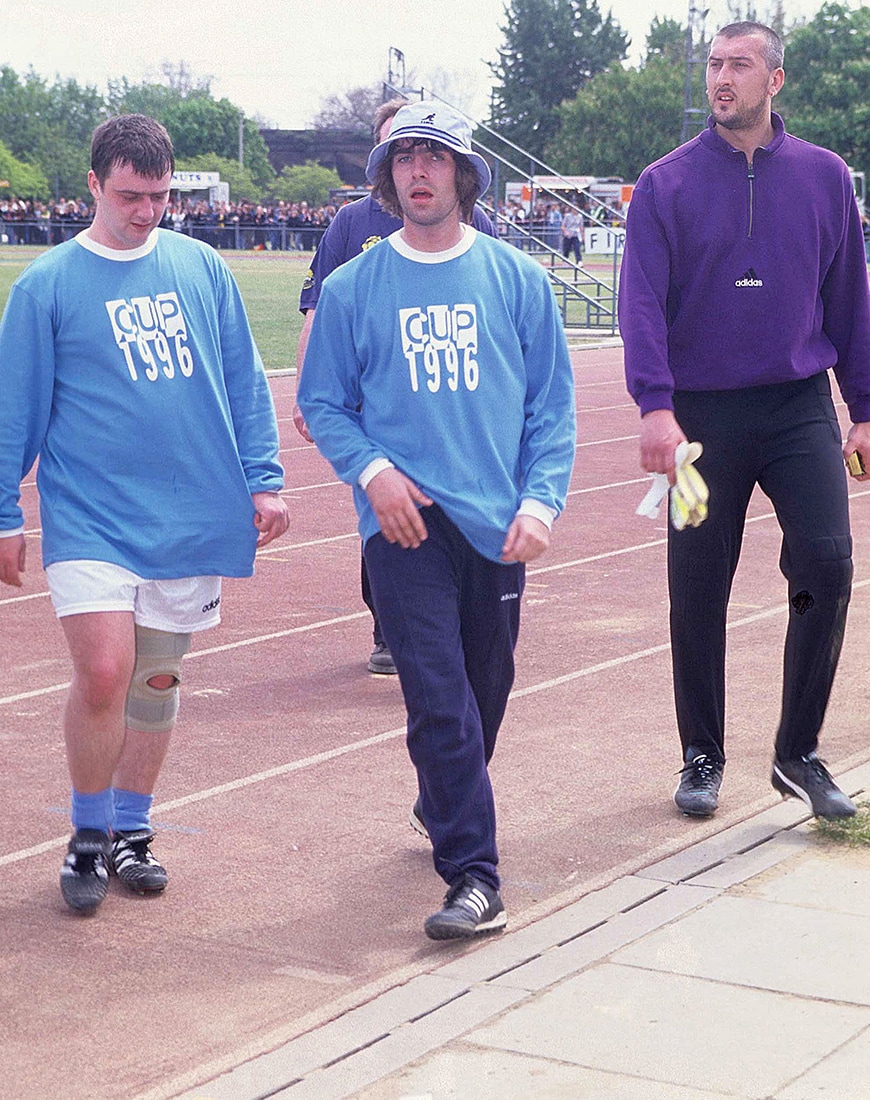 Liam Gallagher and two men wearing athetic wear on a football pitch