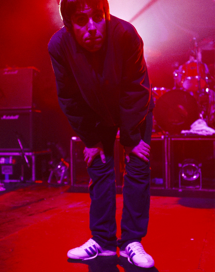 Liam Gallagher wearing white adidas trainers with pink lighting on stage