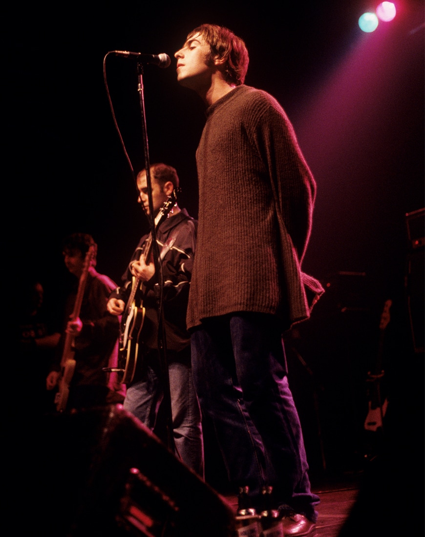 Liam Gallagher wearing a long loose-fitting knit jumper while singing on stage