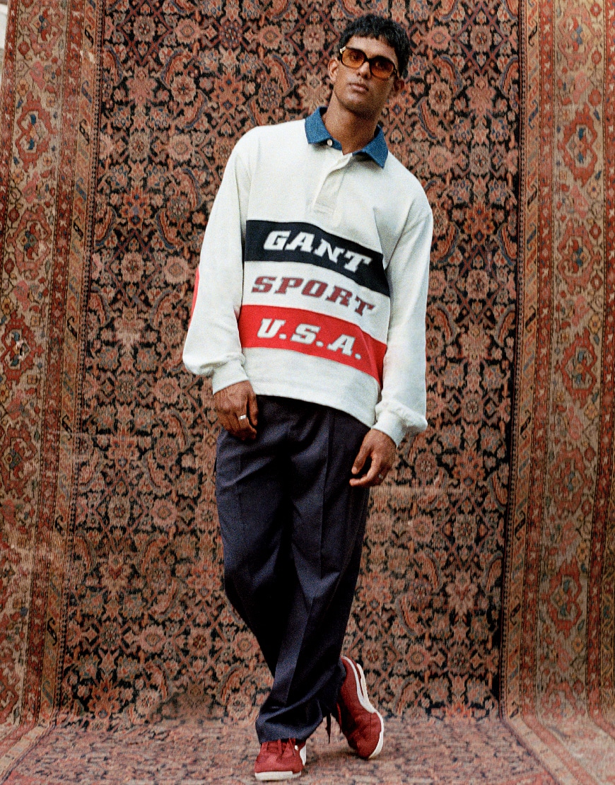 Model wearing dark trousers and white shirt while standing and posing atop a rug