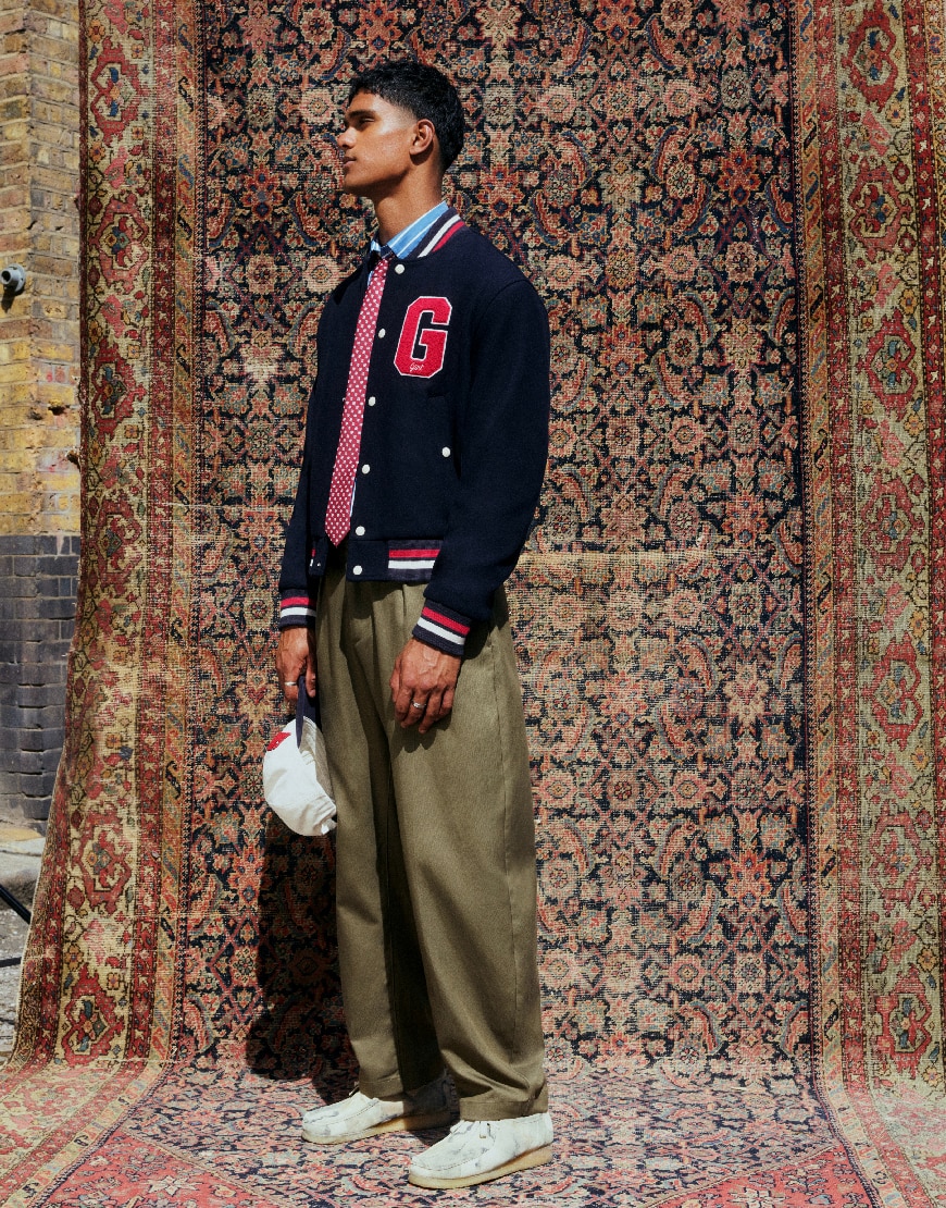 Model wearing brown trousers and navy trousers while standing atop a rug