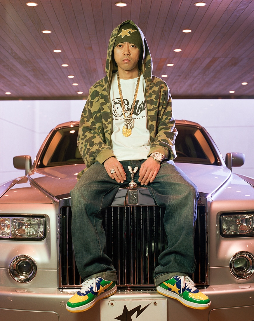 Nigo wearing full BAPE outfit while sitting on top of a white Rolls Royce