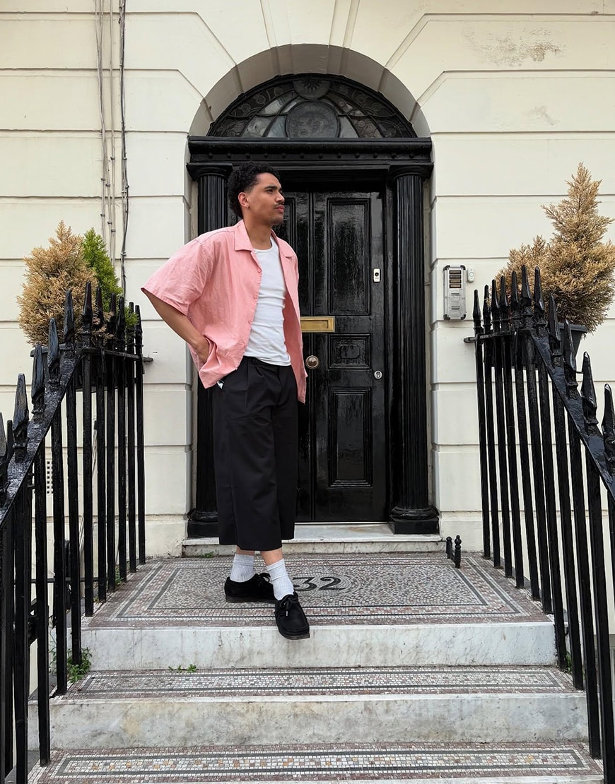 Man wearing a pink shirt and black sorts outside a black door