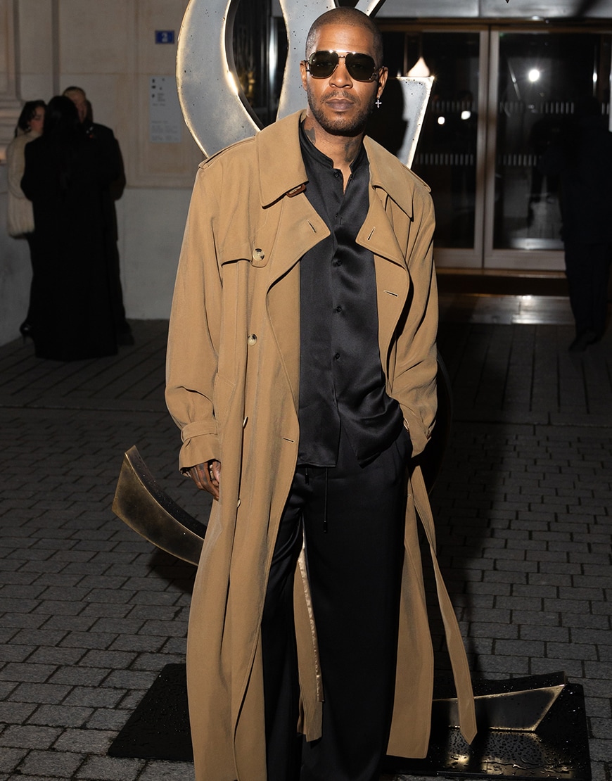 Kid Cudi wearing a brown trench coat and a black silk set