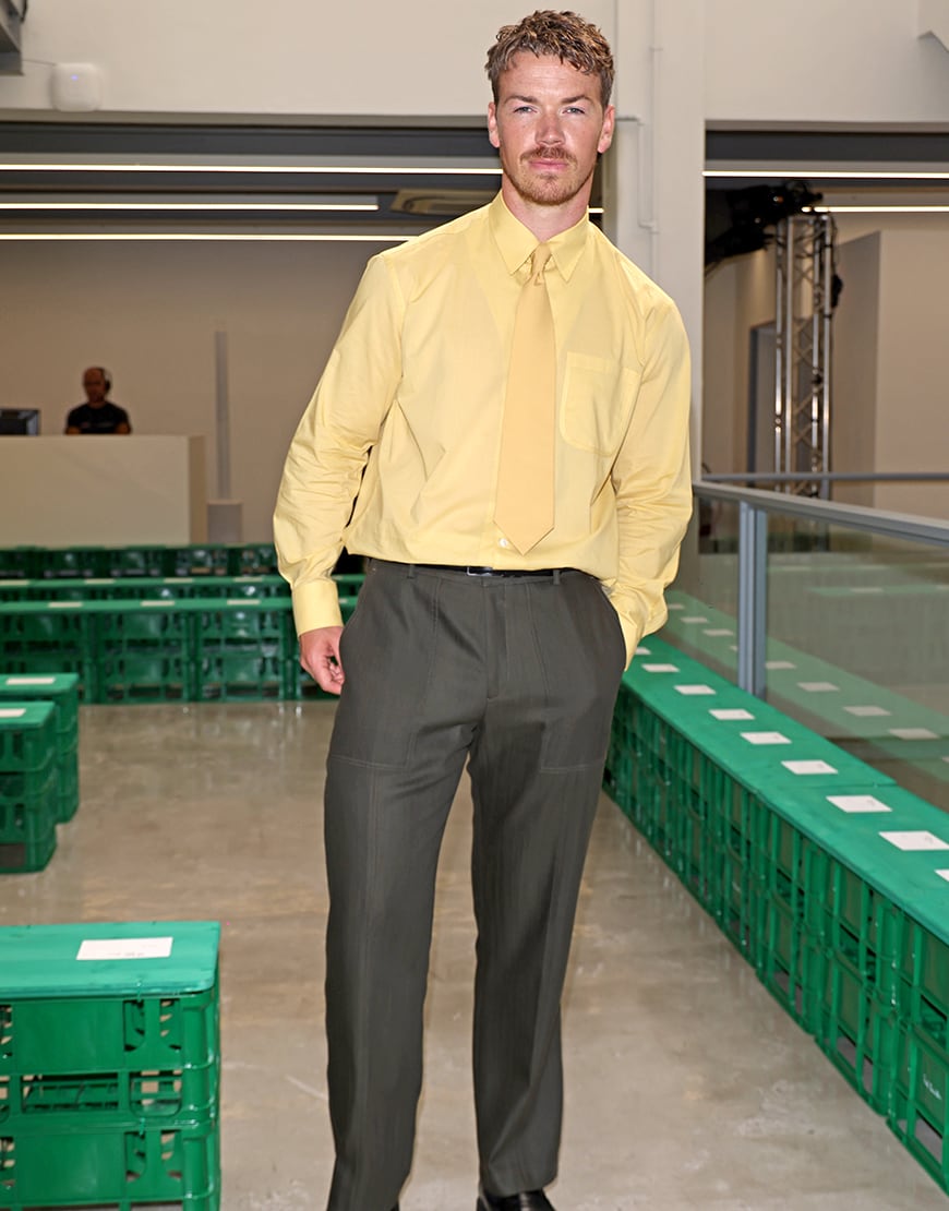 Will Poulter wearing a yellow shirt and grey suit trousers