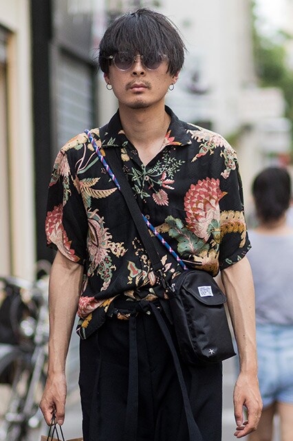 A street-styler wearing a floral-print revere collar shirt, cross-body bag, shades and black trousers | ASOS Style Feed