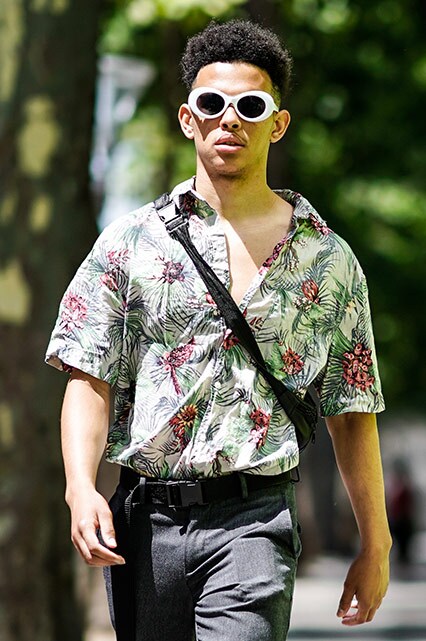 A street-styler wearing white sunglasses, a Hawaiian-print revere collar shirt, grey trousers and Vans Classic trainers | ASOS Style Feed