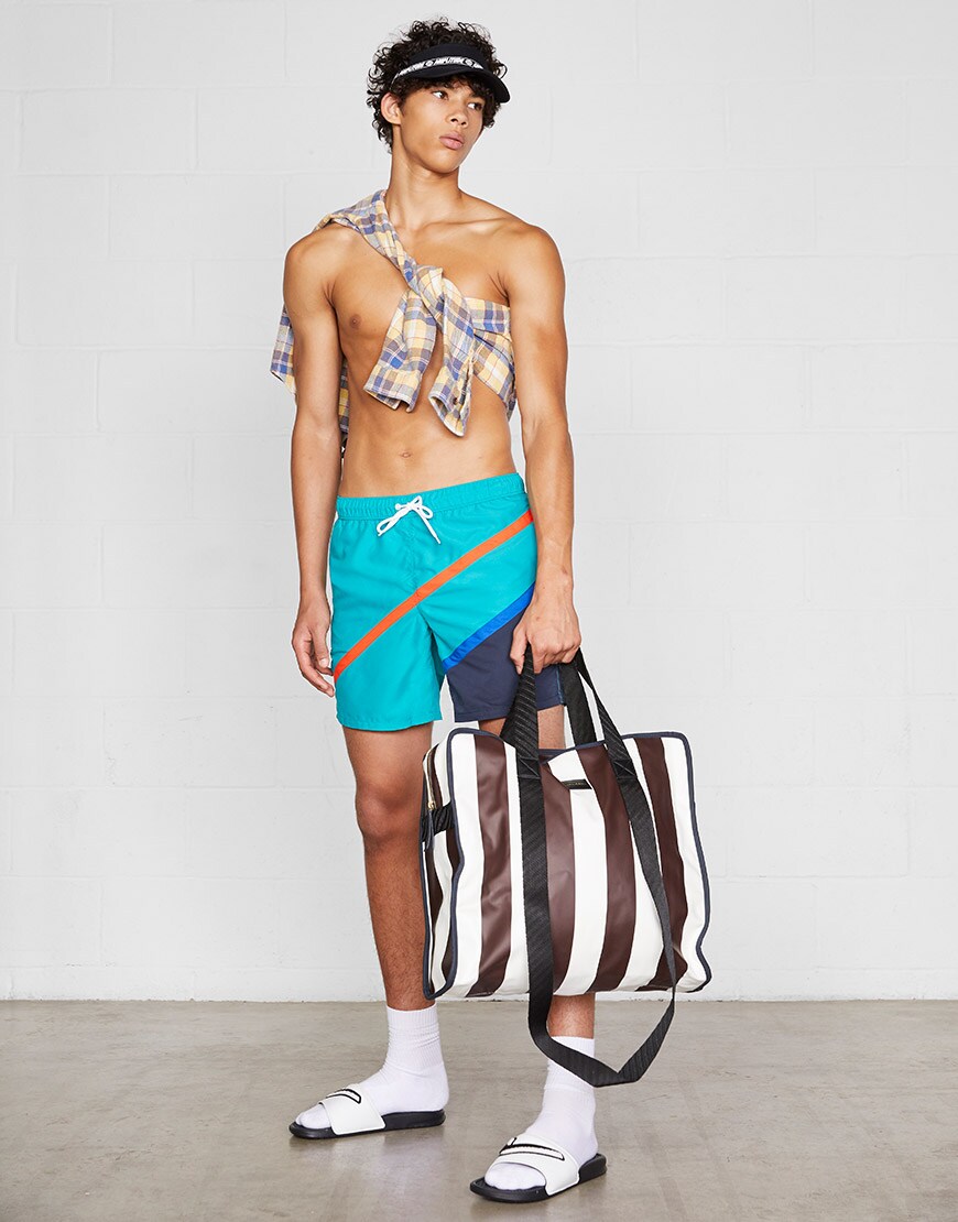 A model wearing a visor, swim shorts, a shirt, socks and sliders and carrying a tote bag | ASOS Style Feed