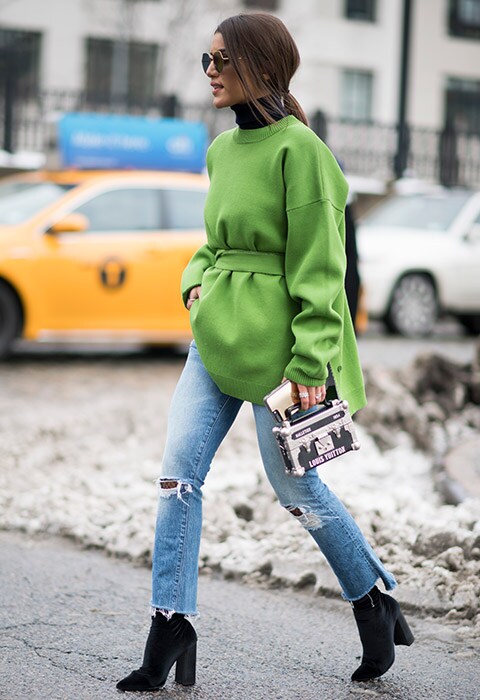 A fashion week attendee wearing a green knit with ripped skinny jeans and black boots.