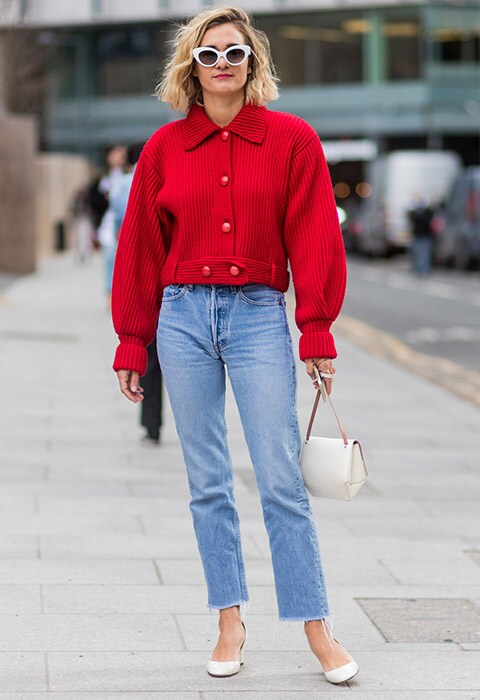 A fashion week attendee wearing a vintage red jacket with straight-leg jeans and white heels.