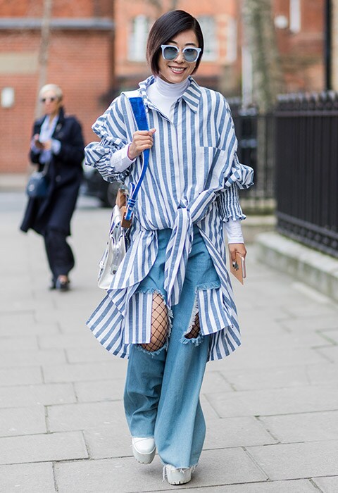 A fashion week attendee wearing an oversized stripe shirt with wide-leg jeans and fishnet tights.