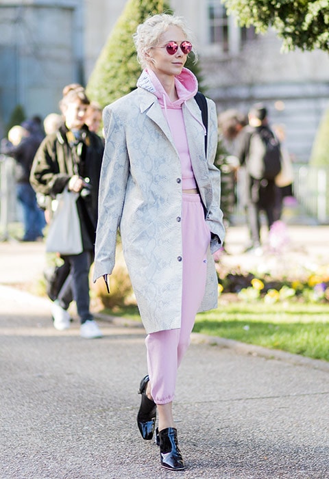 A fashion week attendee wearing a Vetements pink tracksuit with a trench coat and patent boots.
