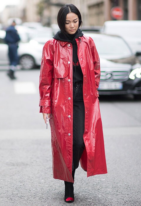 A fashion week attendee wearing a red PVC coat with dark denim jeans and a black hoodie.