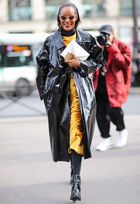 A fashion week attendee wearing a PVC jacket with patent boots and a yellow silky slip dress.